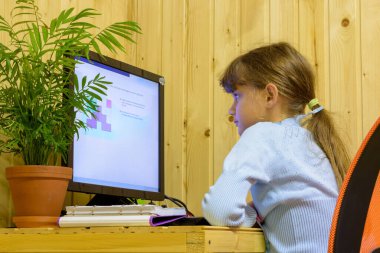A girl solves a problem on a computer during distance learning clipart