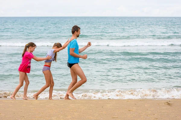 パパと2人の子供は海岸沿いを少し走るのが楽しい ロイヤリティフリーのストック画像