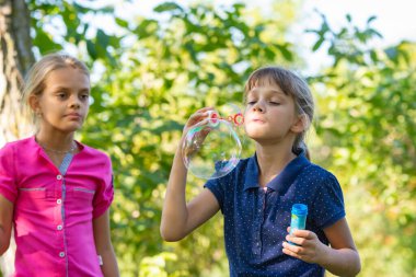 A girl blows bubbles, another girl watches her closely clipart