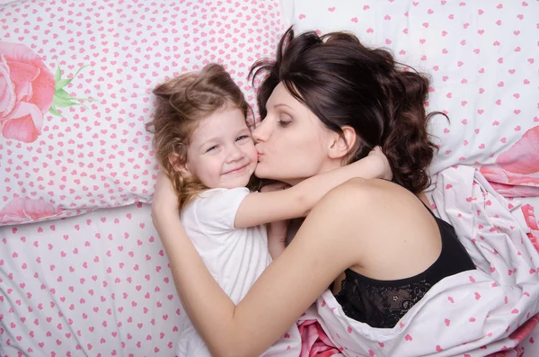 Mamá besa a la hija acostada en la cama — Foto de Stock