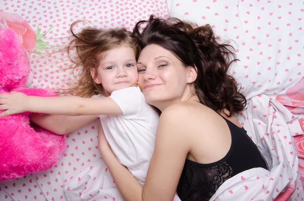 Daughter reaches for a soft toy lying with her mother — Stock Photo, Image