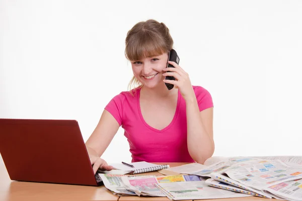 Girl talking on phone while sitting at a table with laptop — Stock Photo, Image