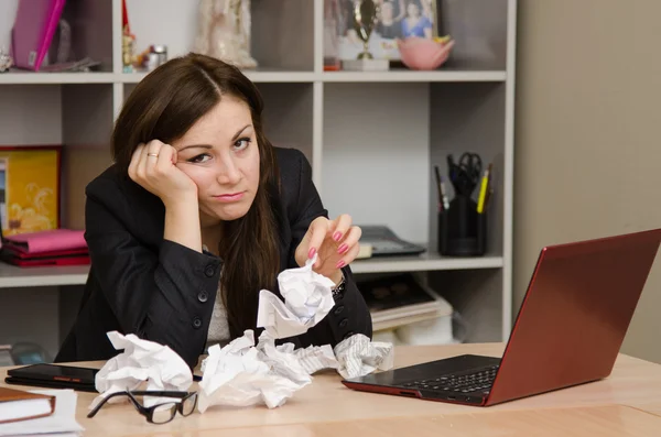 Грустная девушка в офисе с кучей скомканной бумаги — стоковое фото