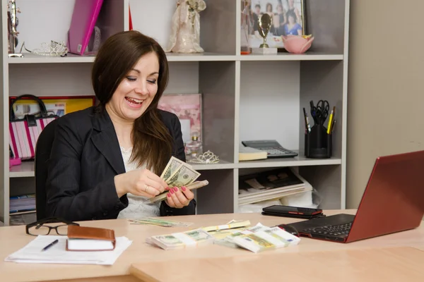 Girl behind desk in office feverishly counts banknotes with a triumphant smile — Stock Photo, Image