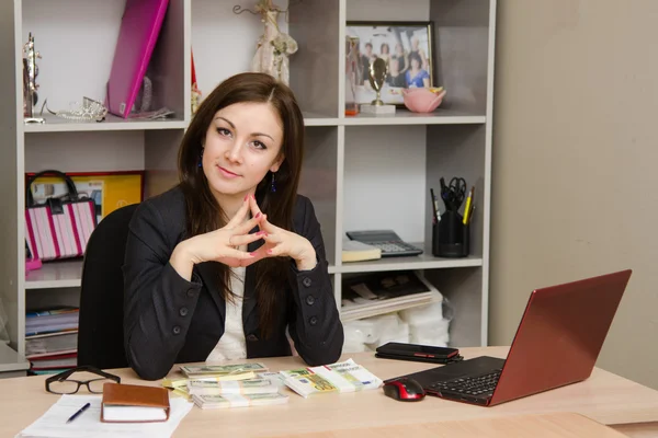 Head girl sitting at a desk with pile money her hands folded in front of him — Stock Photo, Image