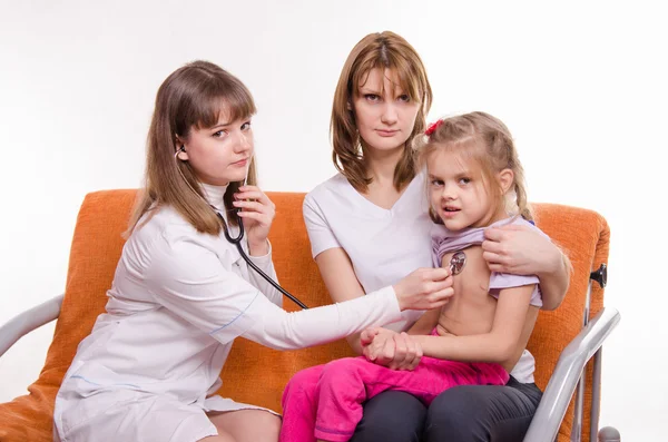 Pediatrician listening stethoscope breast girl sitting on mothers hands Stock Image
