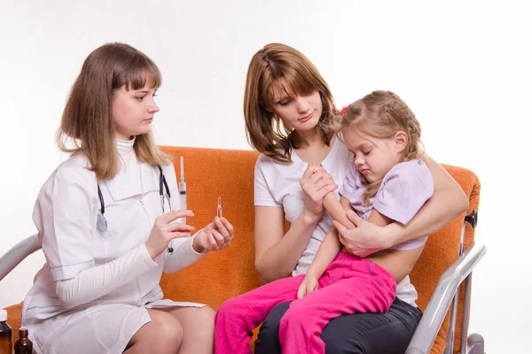 Pediatrician holding a syringe for sick child sitting on hands of mother Stock Photo