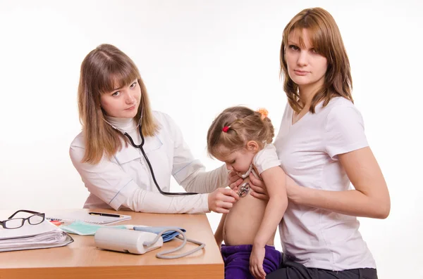 Pediatrician examining a child in the arms of mother Royalty Free Stock Photos