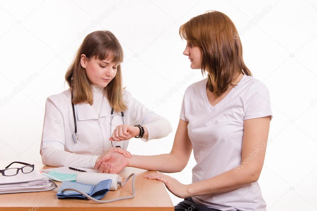 Physician at the table checks the pulse of a patient