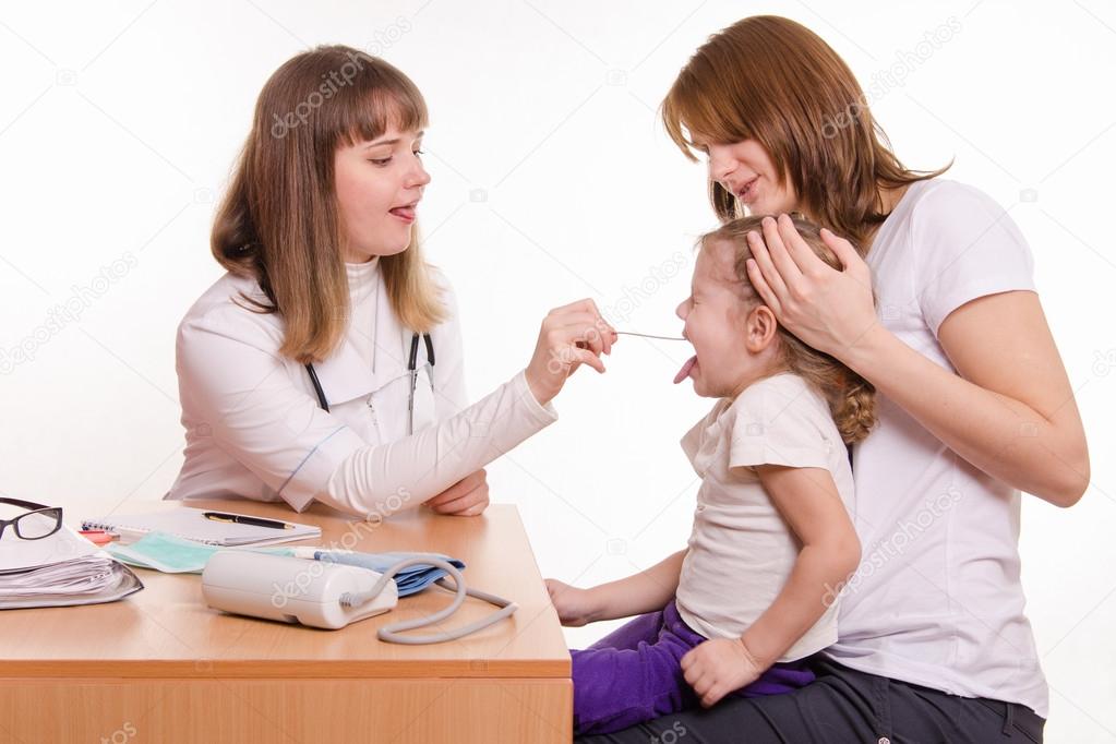 The doctor examines the throat of a child sitting on hands of mother