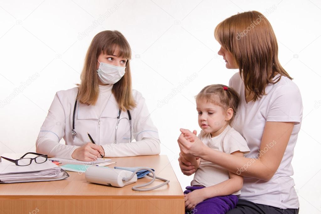 Pediatrician talking in office with a young mother with child on her lap