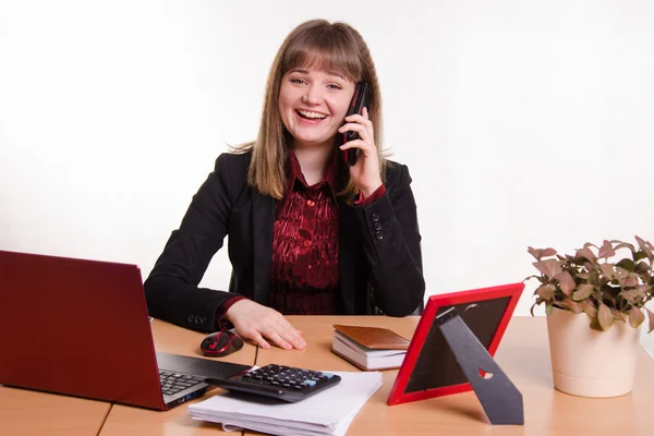 La chica detrás del escritorio de la oficina riendo con el teléfono —  Fotos de Stock