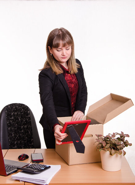 Девушка в офисе собирает, разбирает личные вещи коробку
