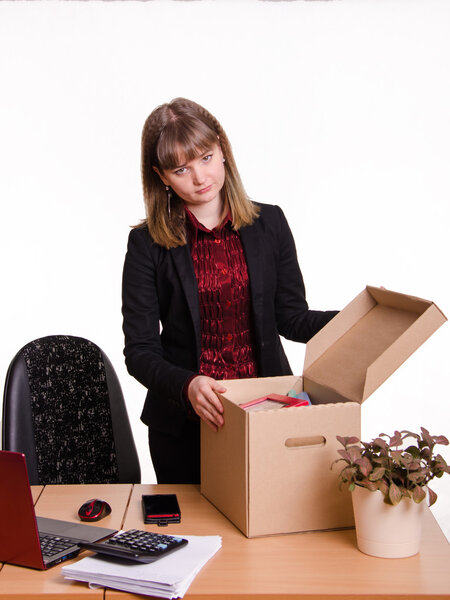 Уволенная девушка в офисе возле стола собирает личные вещи коробка
