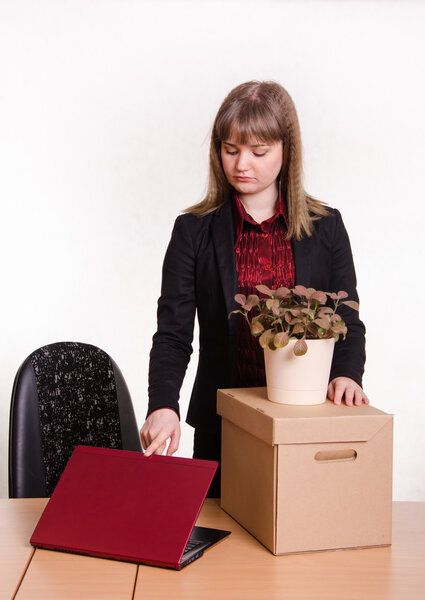 Уволенная девушка в офисе с коробкой и цветами закрывает ноутбук
