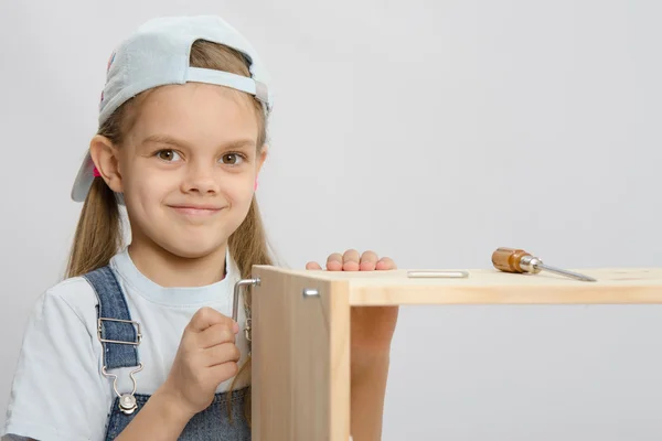 Girl in overalls furniture collector tries to tighten the screw — Stock Photo, Image