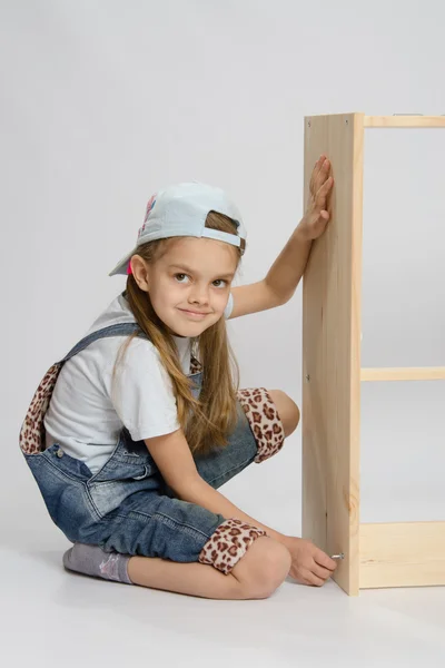 Маленькая девочка в комбинезоне коллекционер мебели поворачивает винт на комоде — стоковое фото