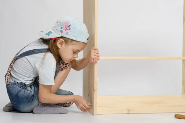 Little girl in overalls collector furniture screw spins — Stock Photo, Image