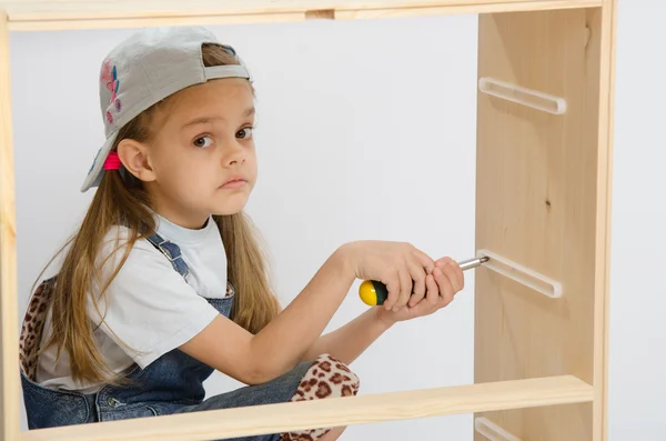 Girl-collector of furniture with a screwdriver collects wooden cabinet — Stock Photo, Image