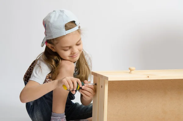 Little girl in overalls collector of furniture screws screwdriver screw — Stock Photo, Image