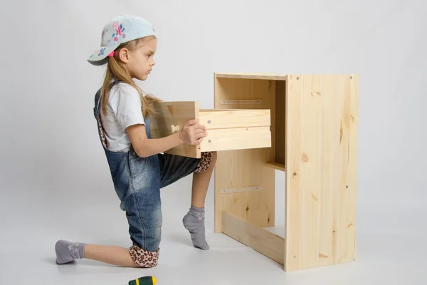 Chica en mono muebles ensamblador inserta una cómoda cajón de cajones —  Fotos de Stock