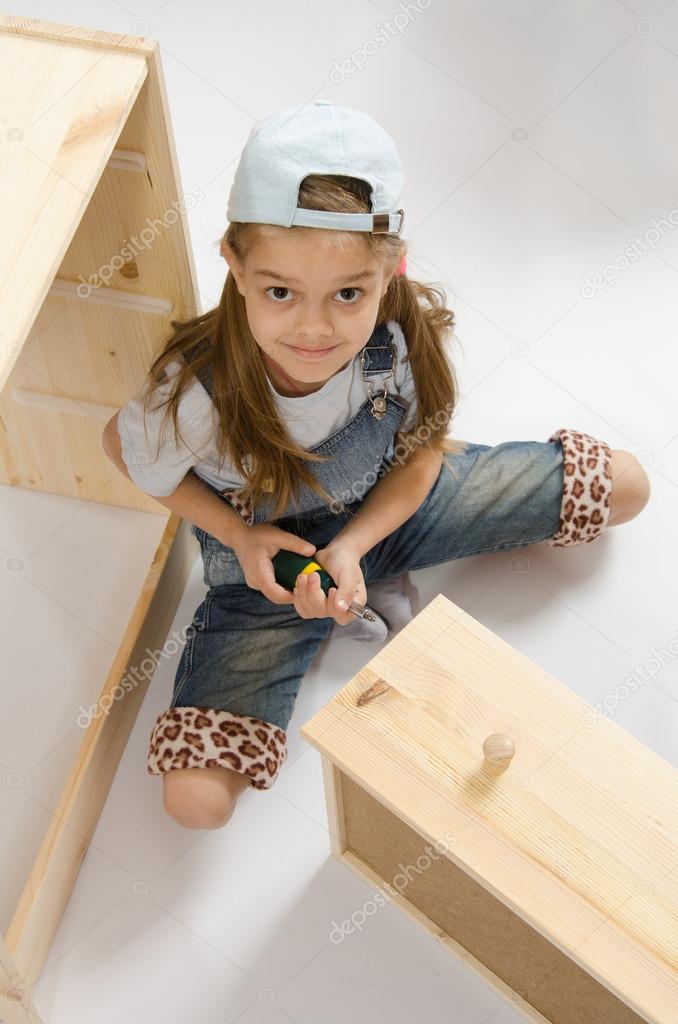 Little girl in overalls collector furniture spins screwdriver