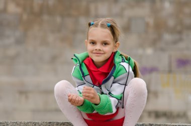 Altı yıl yaşlı kız bir granit duvar arka plan üzerinde çömeldi.