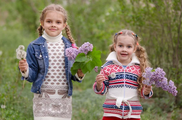Twee meisjes met paardebloemen en seringen — Stockfoto