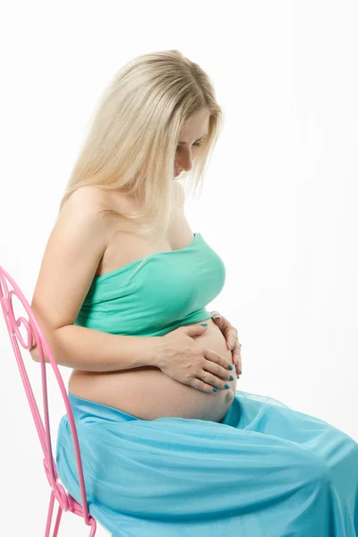 Schwangere junge Frau sitzt auf einem Stuhl und blickt auf den Bauch — Stockfoto