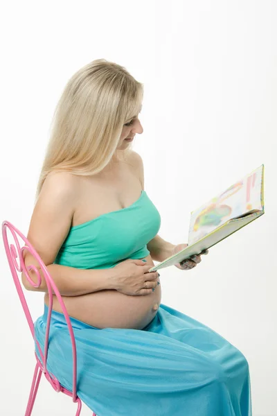 Giovane donna incinta che legge un libro seduta sulla sedia — Foto Stock