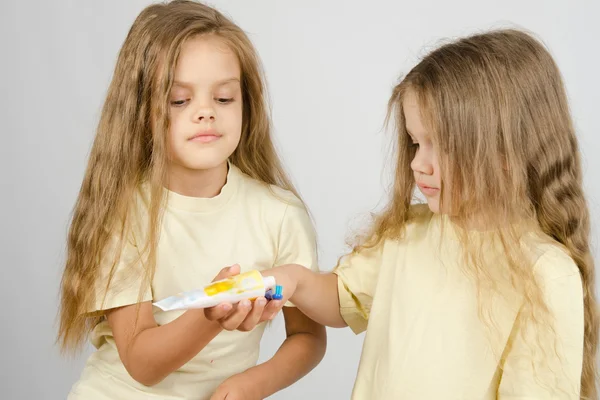 Chica exprimiendo pasta de dientes de una hermana tubo —  Fotos de Stock