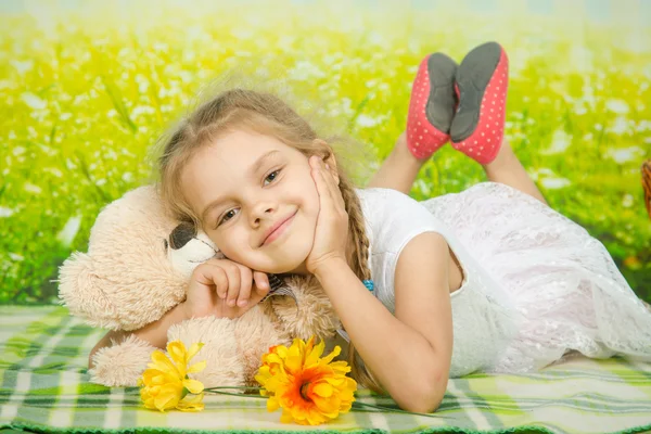 Five-year girl hugging a teddy bear lying on picnic rug — 图库照片