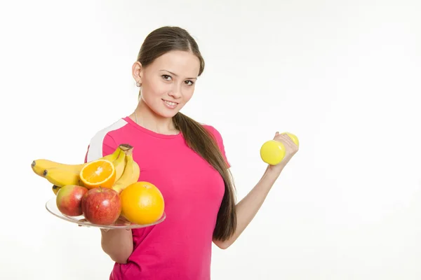 Trzymając płytkę z owoców i hantle lekkoatletka dziewczyna — Zdjęcie stockowe