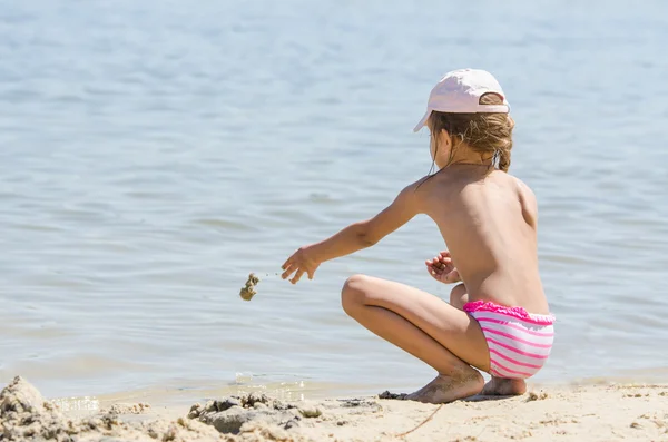 Girl on the river throws sand in water — Stock Photo, Image