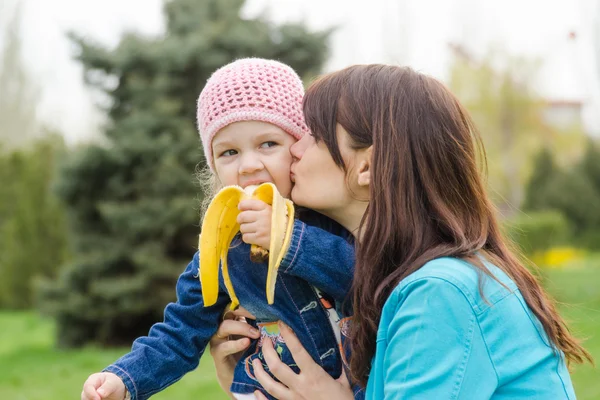 Mamma kysser den flicka som äter en banan på picknick — Stockfoto