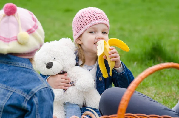 Ragazza su picnic mangia una banana e tiene orso — Foto Stock