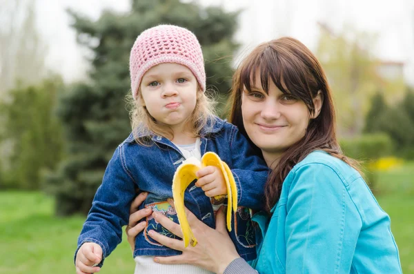 Mamá mantiene chica que come un plátano en el picnic —  Fotos de Stock
