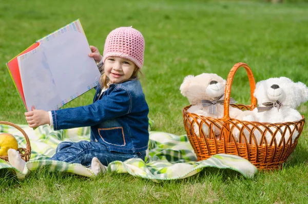 Šťastná dívka ukazuje knihu na piknik — Stock fotografie