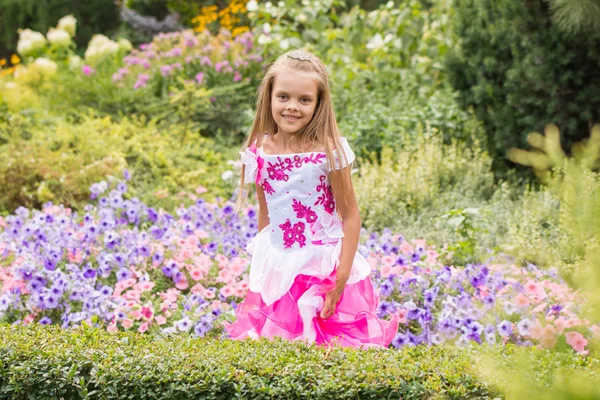 Happy little girl in a long dress at flower bed — Stock Photo, Image