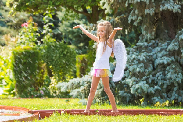 Chica con alas de ángel en el jardín disfruta de salpicaduras de agua — Foto de Stock