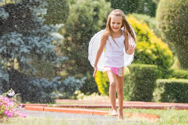 Menina com asas de anjo correndo ao redor na chuva no jardim — Fotografia de Stock