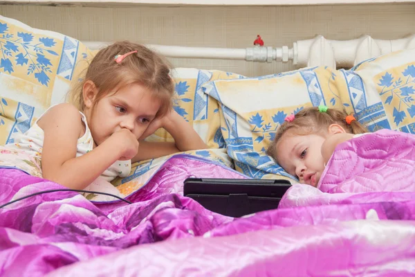 Two girls lying in bed looking at a tablet computer — Stock Photo, Image