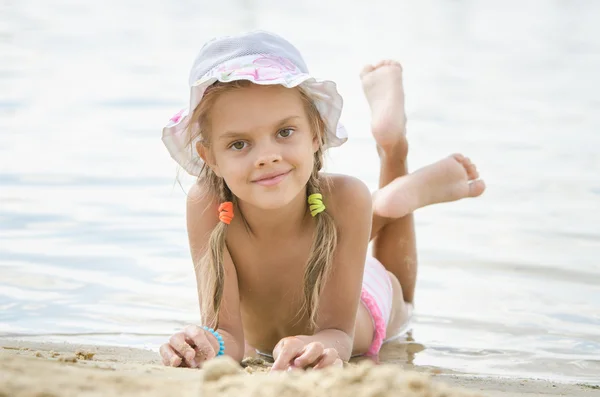 Шестилетняя девочка лежит на песке на пляже — стоковое фото