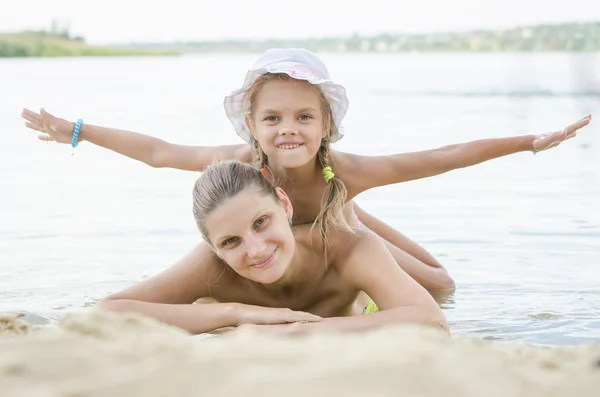 Moeder en dochter liggend op het zand aan de oever van de rivier — Stockfoto