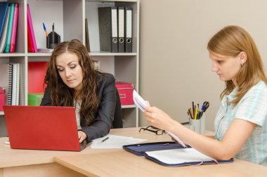 The specialist works in the laptop, the visitor leafing through paper documents
