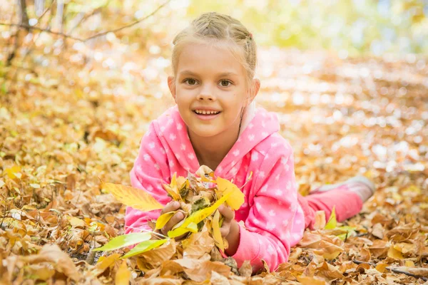 Шестилетняя девочка лежит на желтых опавших листьях — стоковое фото