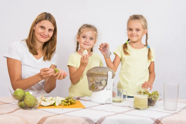 Mother and daughter squeezing juice from pears and grapes — Stock Photo, Image