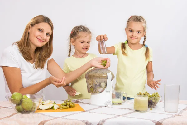 She and her two daughters squeezed juice in a juicer — Stock Photo, Image