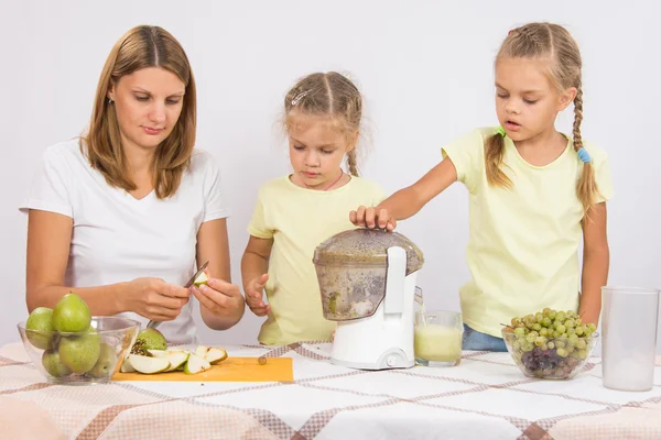 Mom cut pear juice, the children throw them in a juicer — Stock Photo, Image