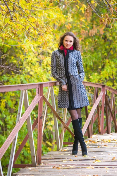Молодая девушка прислонилась к забору старого моста в осеннем лесу — стоковое фото